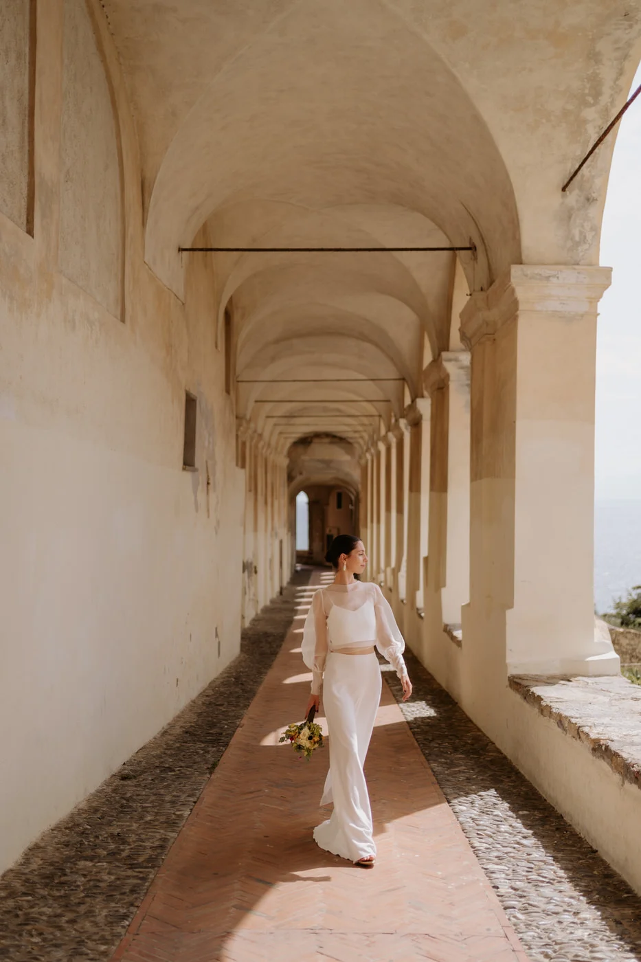 Bride with her bouquet walking under an arched portico