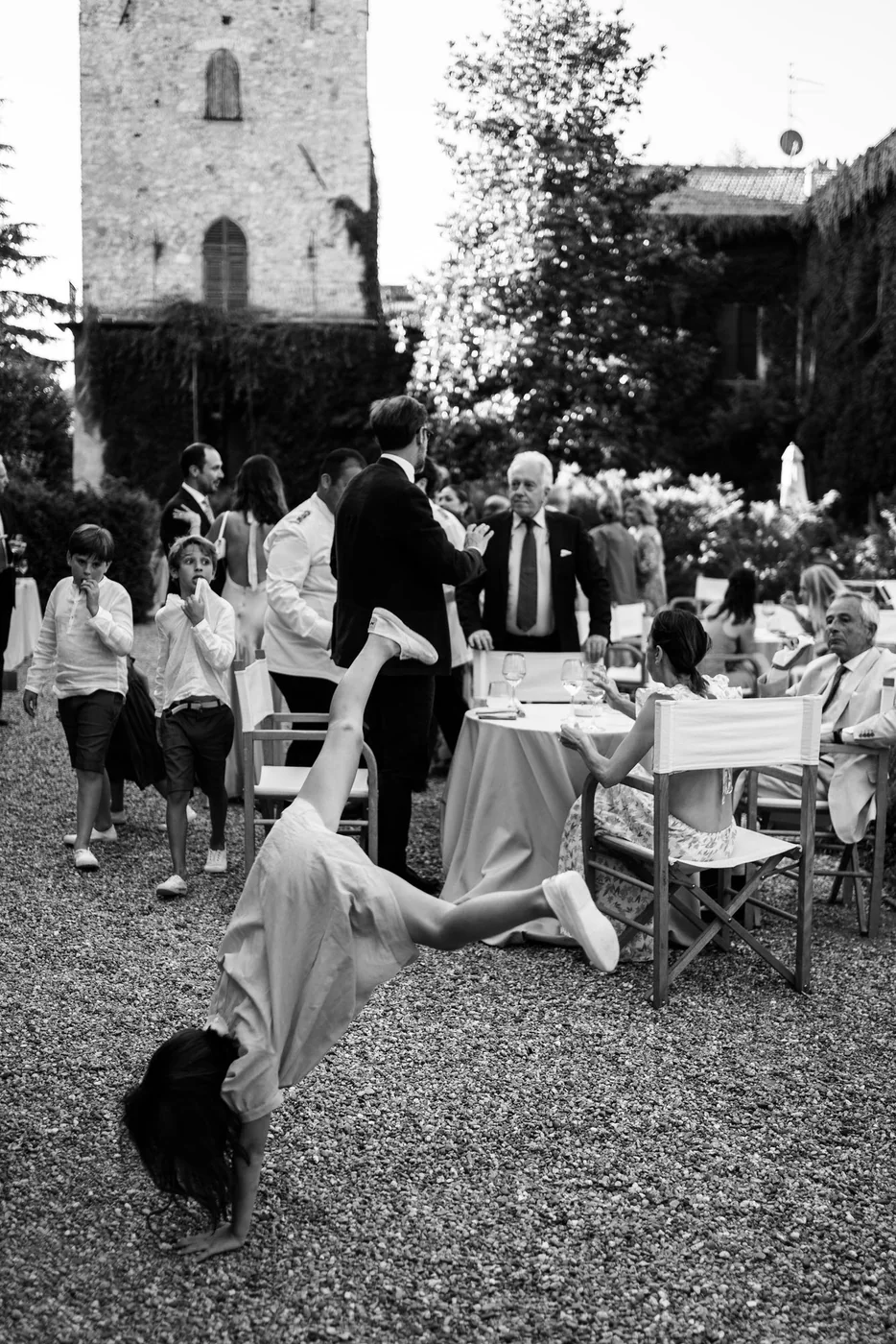 Little girl doing a handstand among the guests during the reception, black and white photo