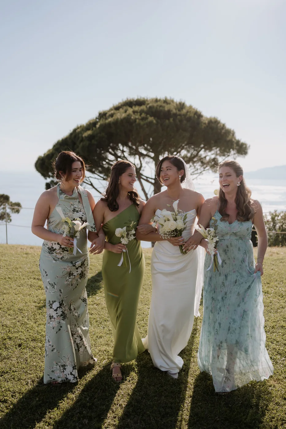 The bride with her bridesmaids in green and blue on the lawn overlooking the sea