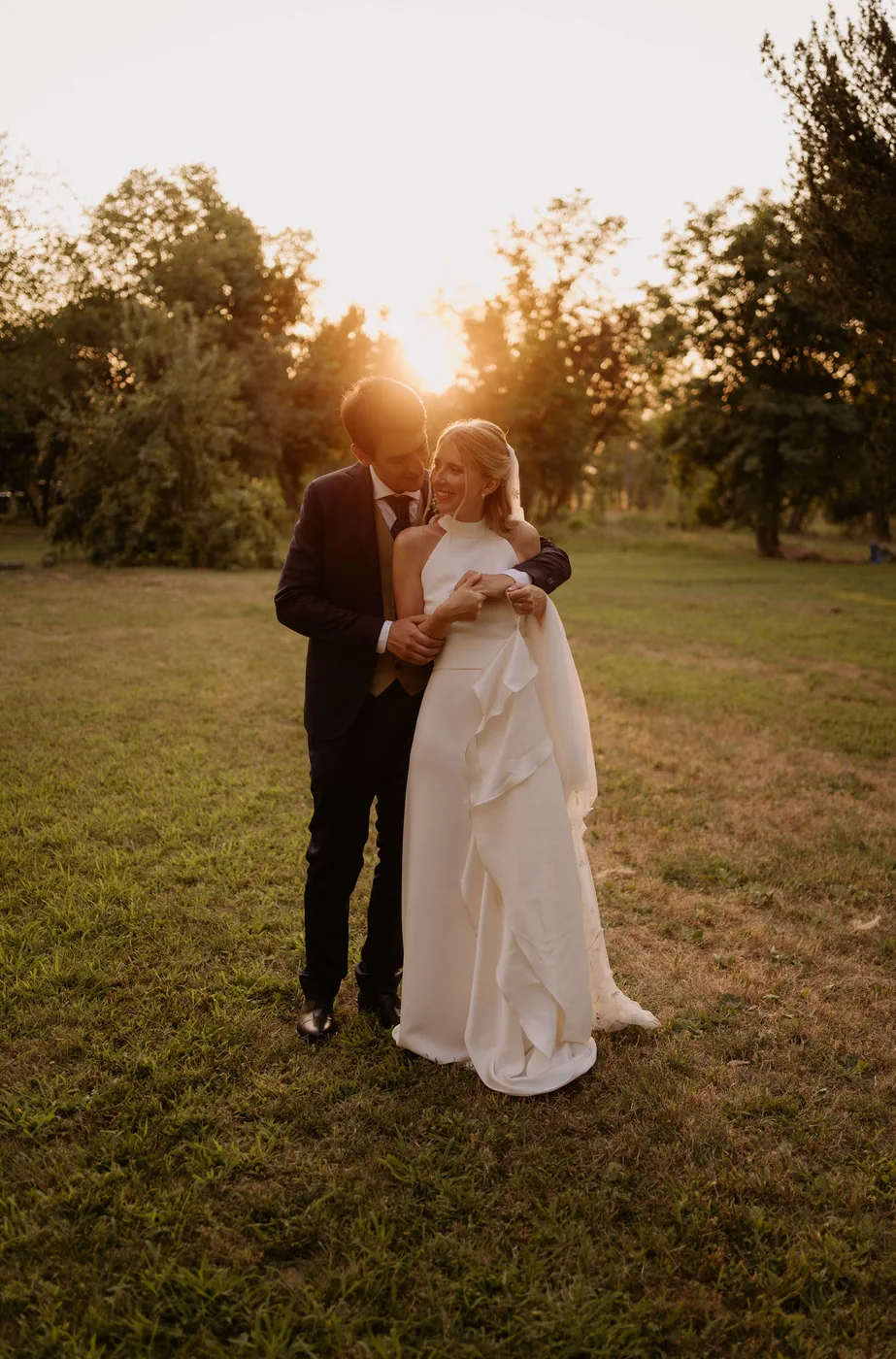 Bride and groom embracing on a lawn at sunset