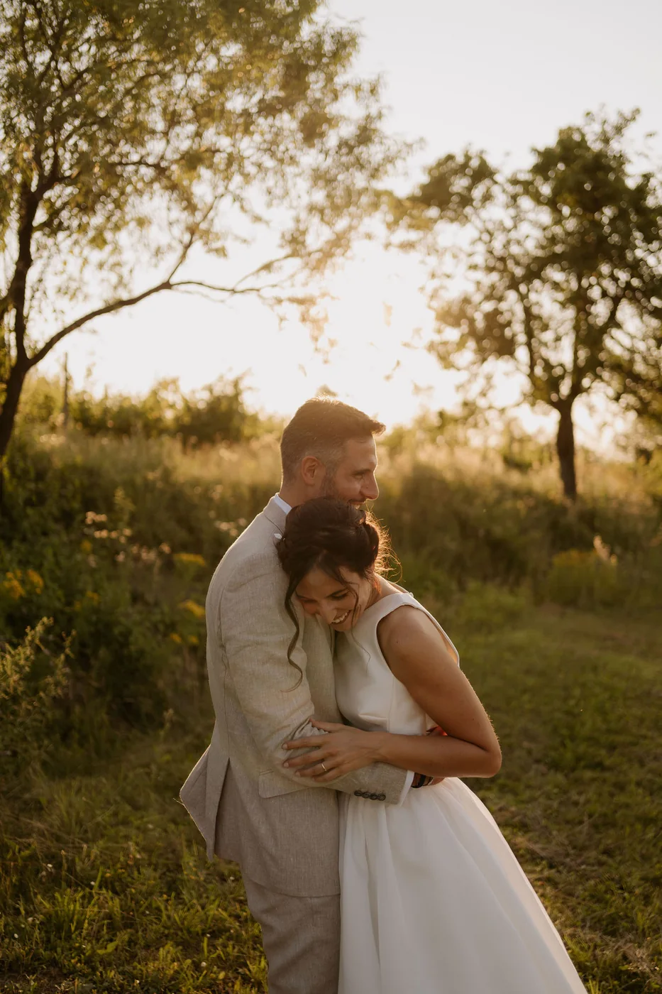 Bride and groom embracing in a meadow among the trees at sunset