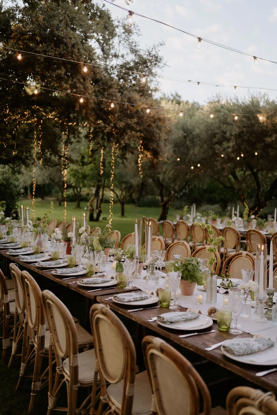 Reception table set outdoors among the trees under hanging lights