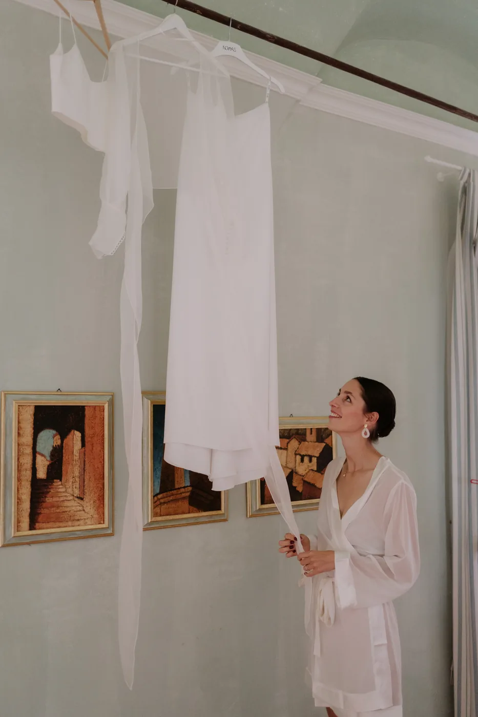 Charlotte, the bride, looking at her dress hanging in the getting ready room in Cervo