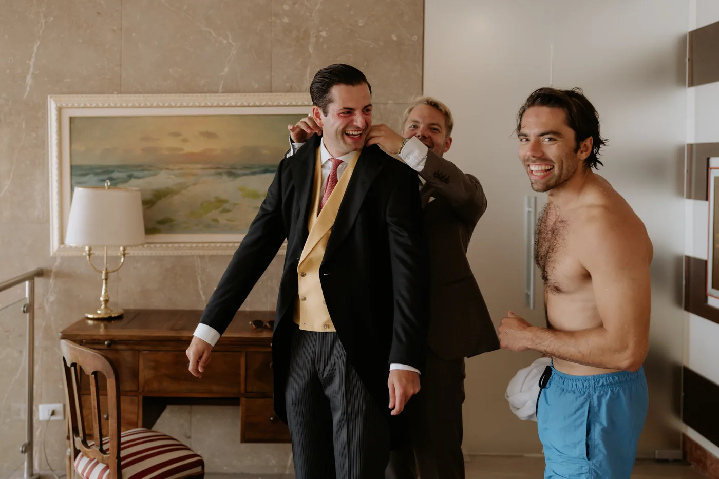 The groom putting on his jacket with his friends' help, amid laughter