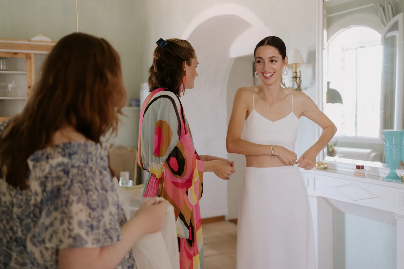 The bride in her two piece dress smiling at her friends in the bright room