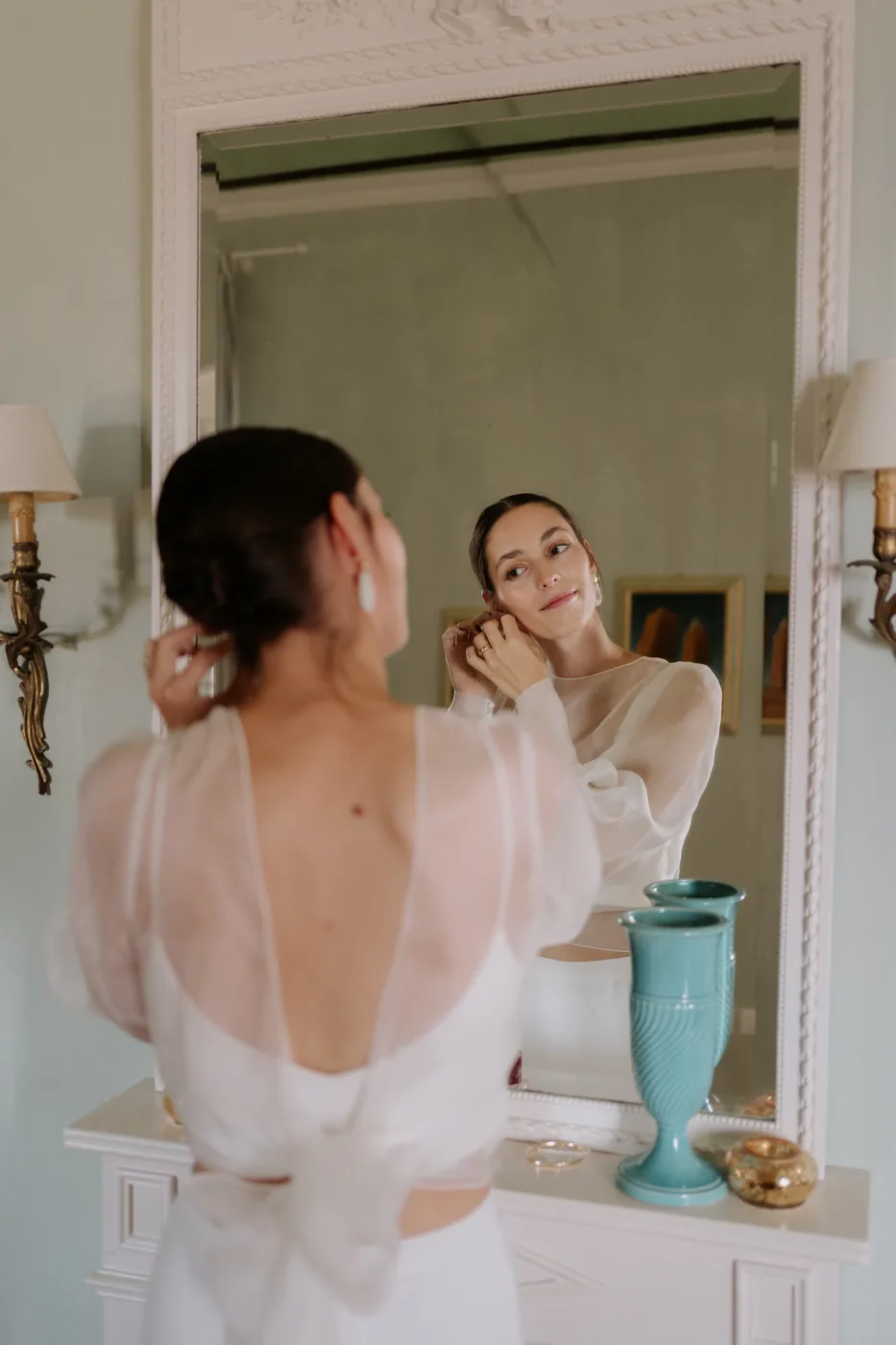The bride putting on her earrings in front of the mirror