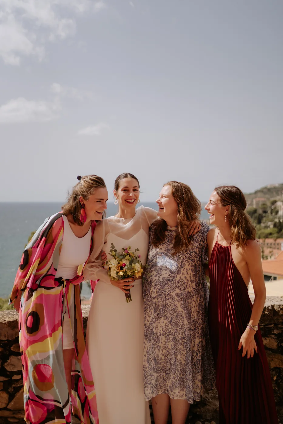 The bride with her bouquet laughing with her friends on the lookout over the sea