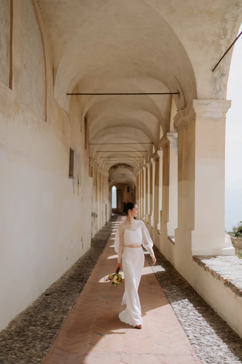 The bride walking under the long portico in Cervo