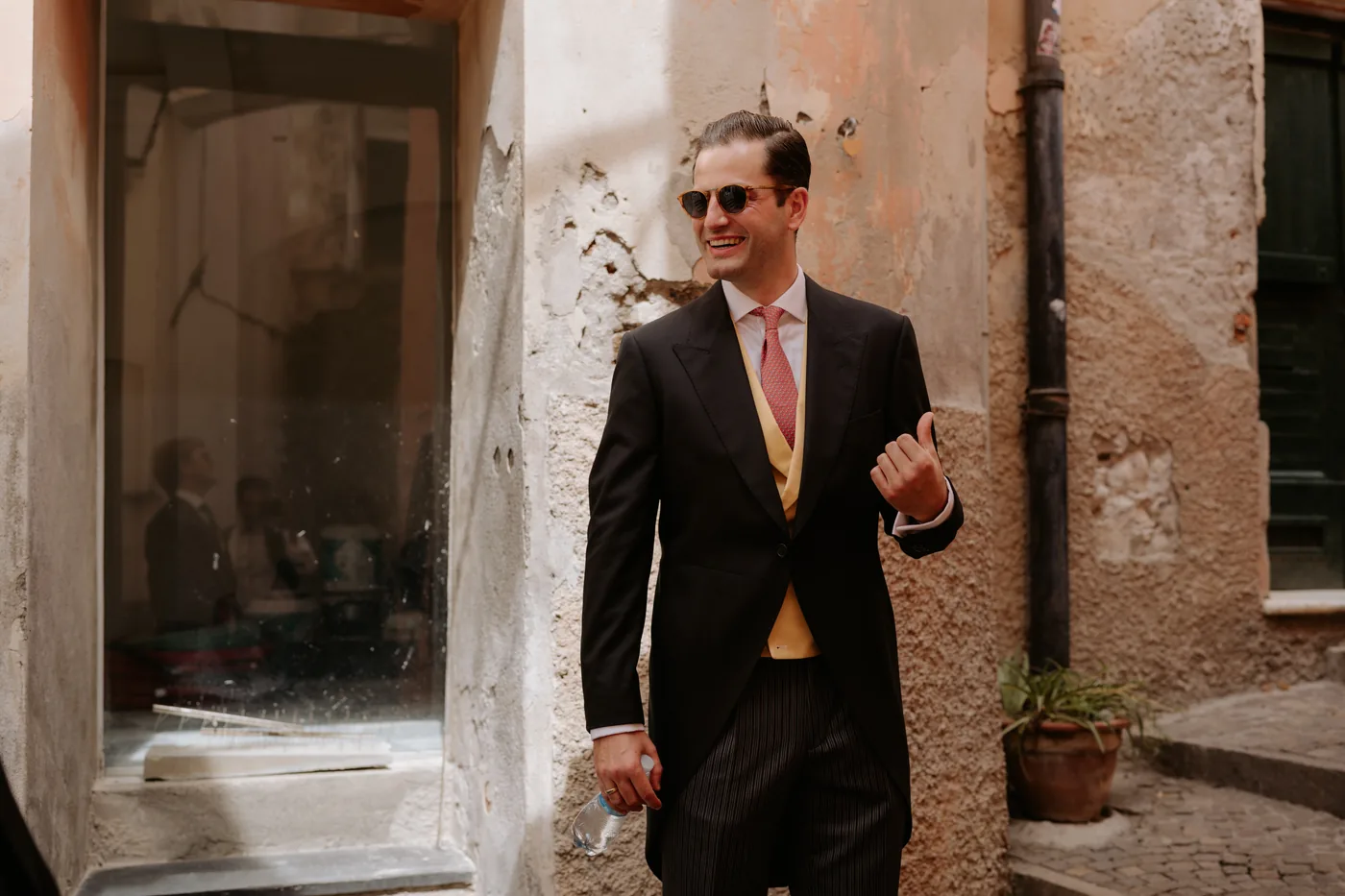 The groom in a morning suit smiling in the stone lanes of Cervo