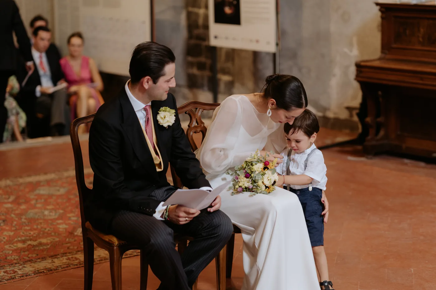 The couple smiling at a little boy sitting beside them during the ceremony