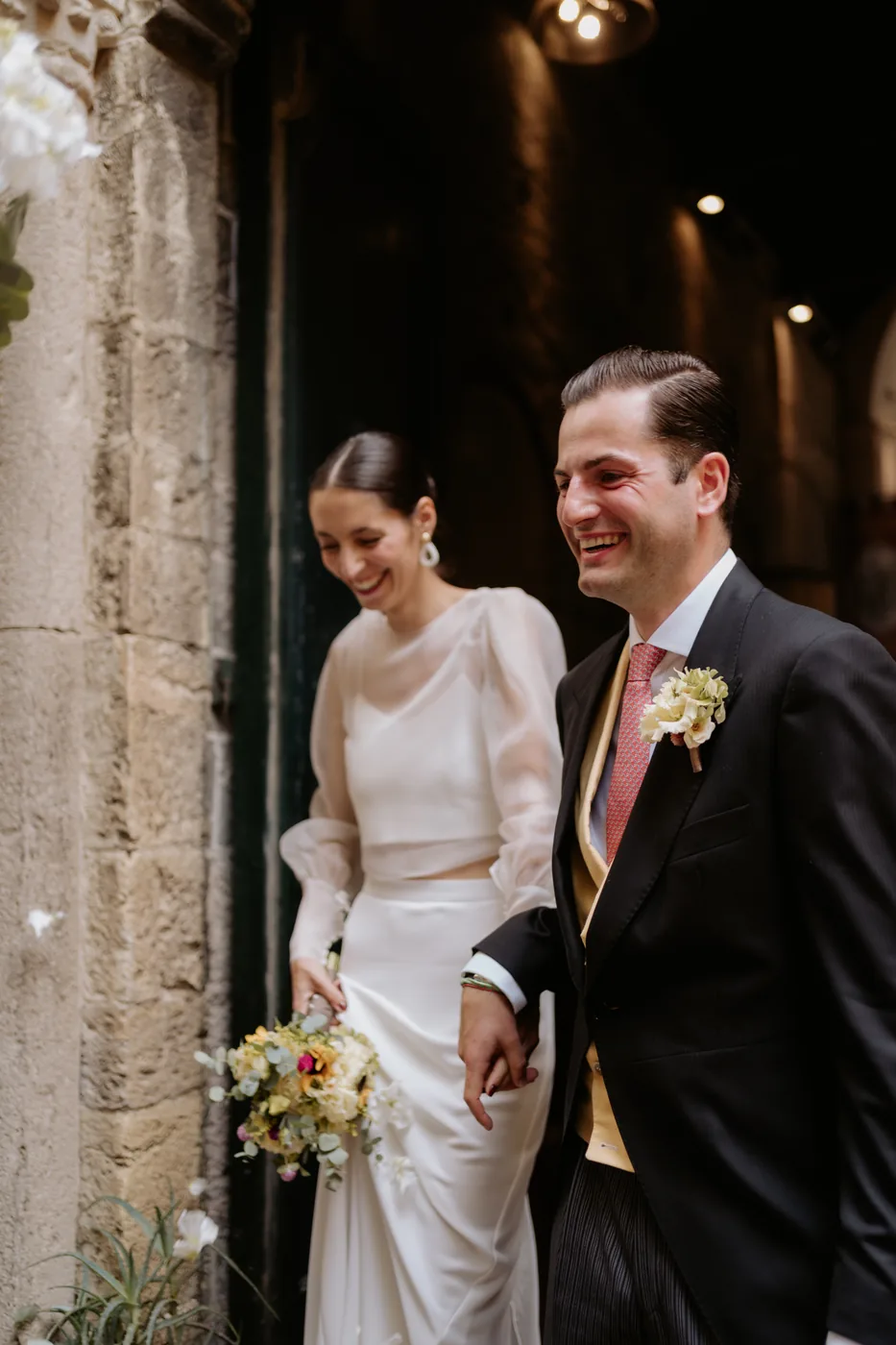 The couple smiling as they come out of the stone doorway after the ceremony