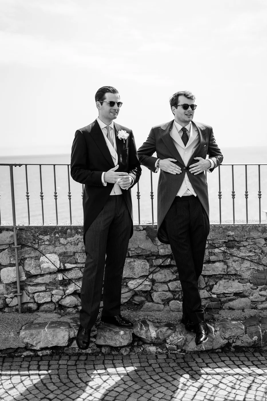 The groom and a friend in morning suits and sunglasses, in black and white