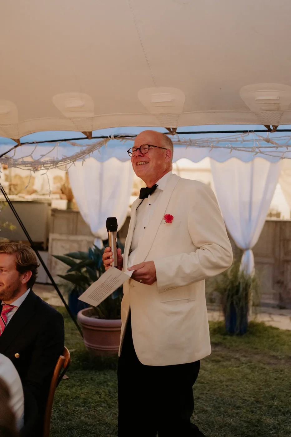 A guest in a white tuxedo giving a speech under the gazebo