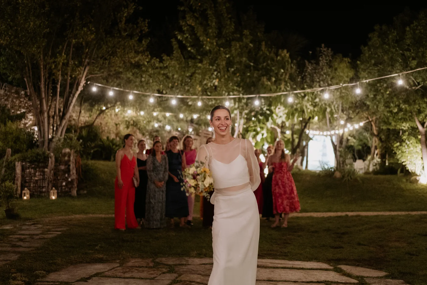 The bride with her bouquet in front of her friends under the string lights