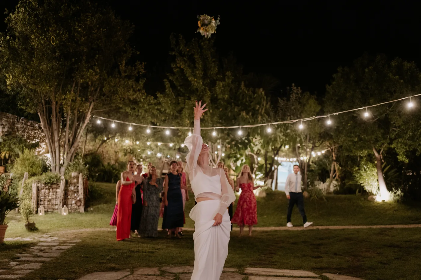 The bouquet toss in the garden lit by string lights