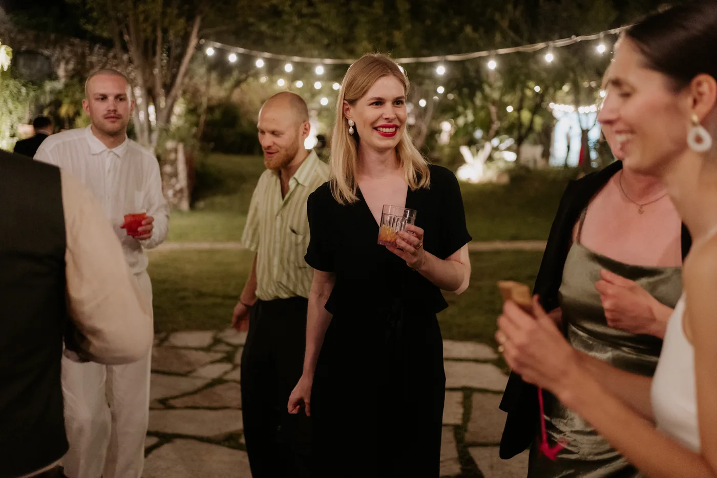 Smiling guests with their drinks under the string lights