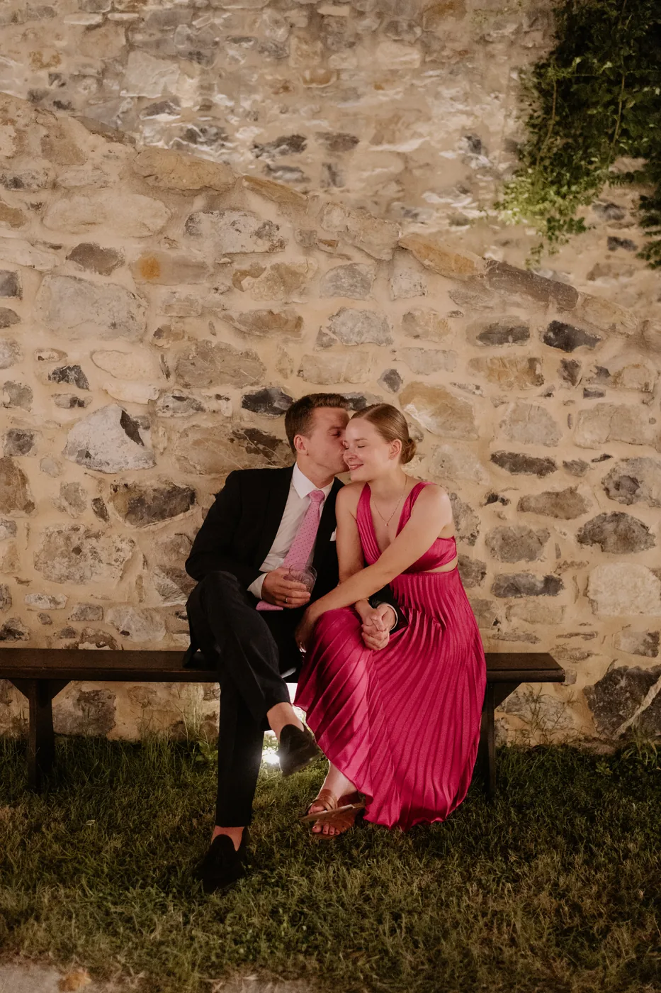 Two guests embracing on a bench against the stone wall