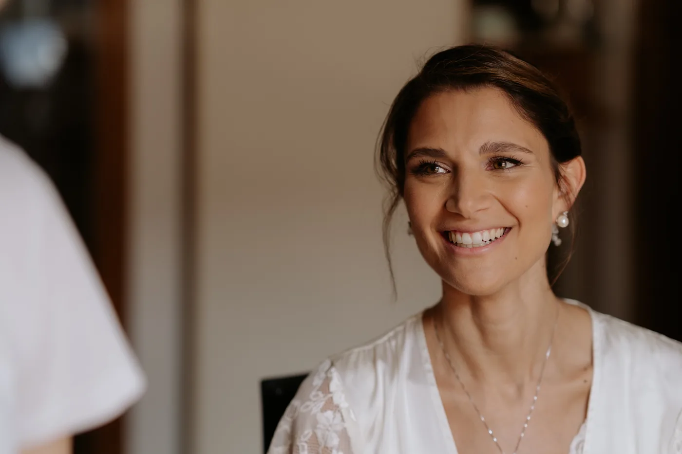 The bride smiling while getting ready, in a white robe
