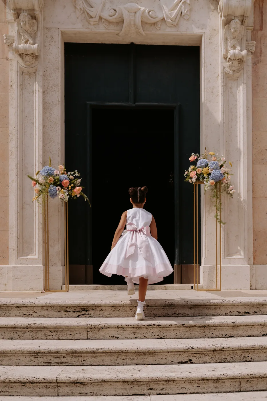 A little girl in a white dress climbing the steps toward the church doorway