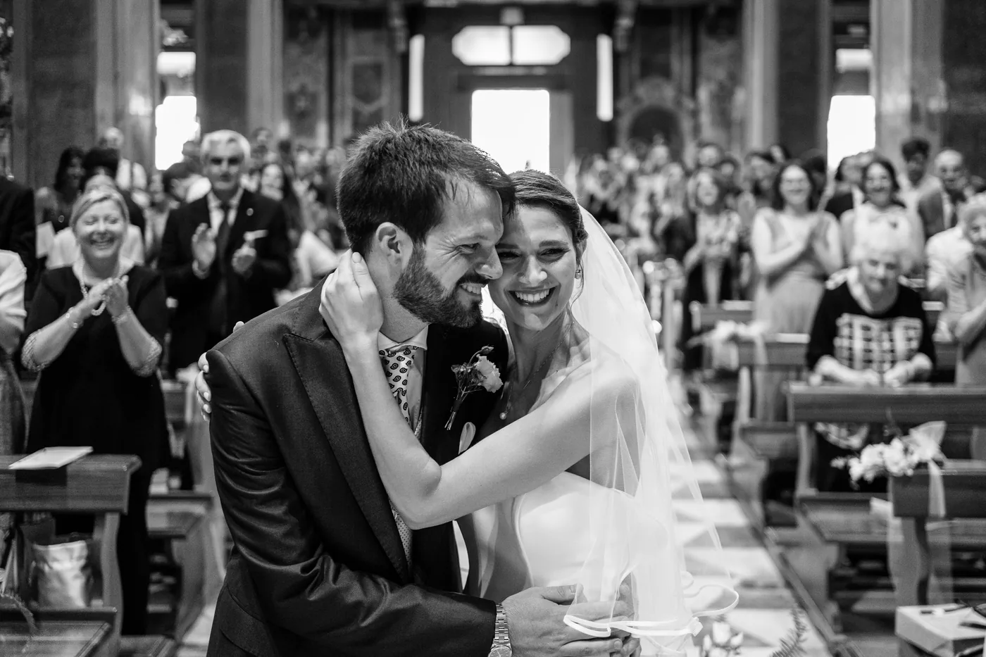 The couple embracing among the guests in church, in black and white