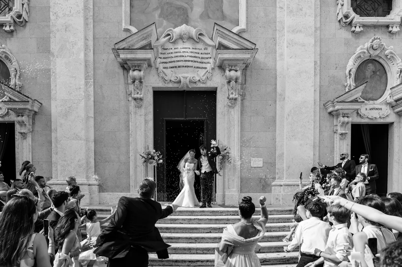 The couple leaving the church among celebrating guests, in black and white