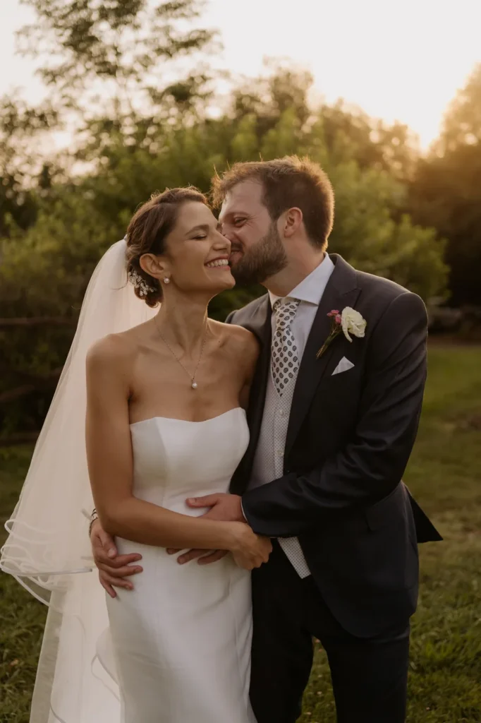 The groom kissing the bride on the cheek in the late afternoon light