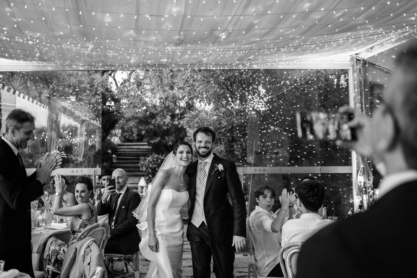 The couple's entrance to dinner under the string lights, in black and white
