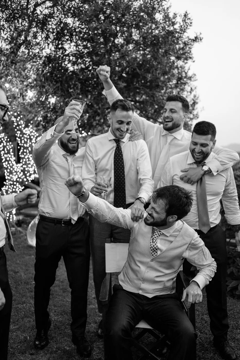 The groom's friends celebrating by lifting him up in the garden, in black and white