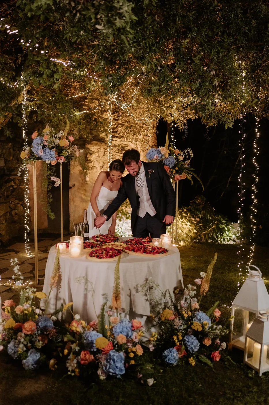 Cutting the cake under an arch of flowers and lanterns