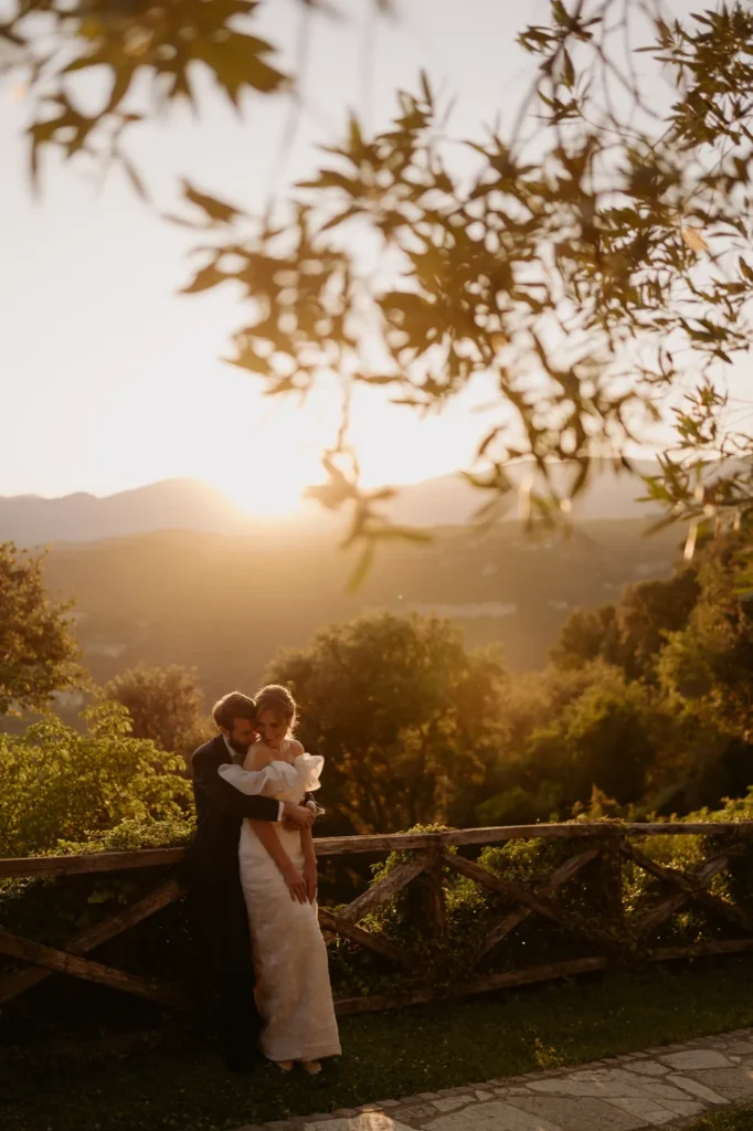 The couple embracing by the fence with the hills at sunset