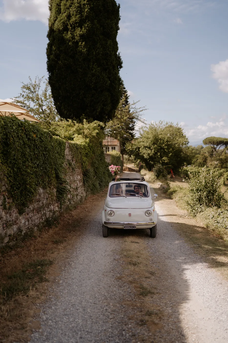 The white Fiat 500 driving down the dirt road toward the villa